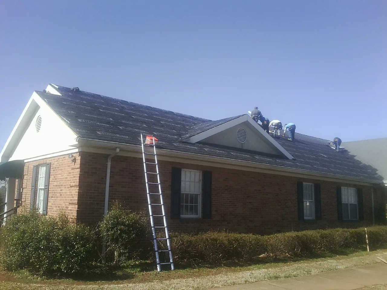 Crew tearing shingles off a brick ranch roof with a ladder set — Metal Roof Repair work by our crew in Sunland