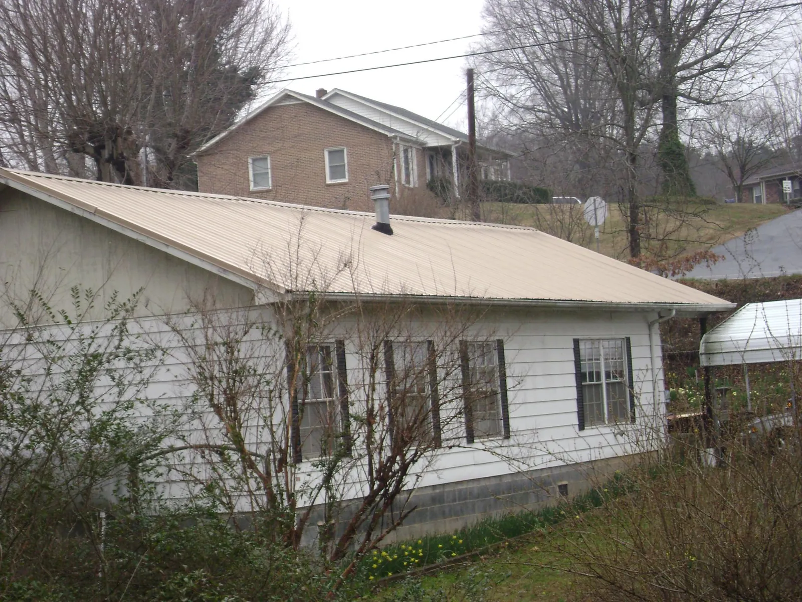 Tan metal roof on a white sided house set into a hillside — Commercial Roofing by Roofing Brothers in Sunland
